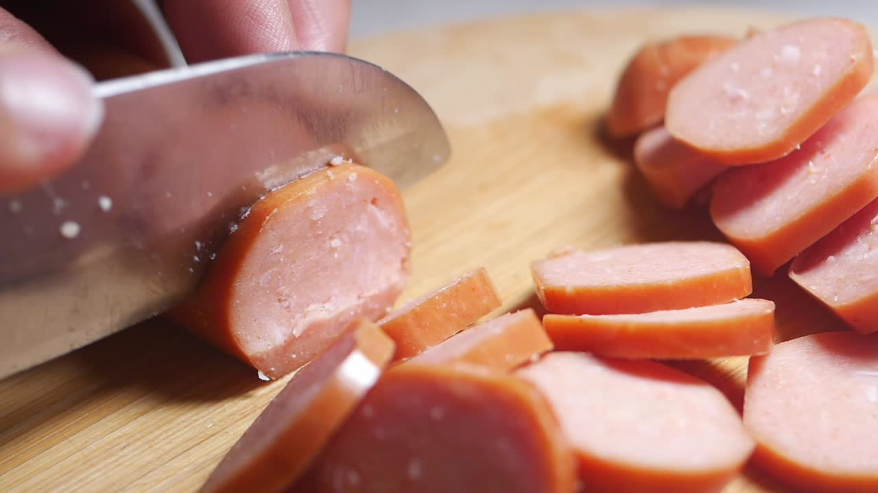 Primo piano di una mano che taglia una salsiccia su un tagliere di legno