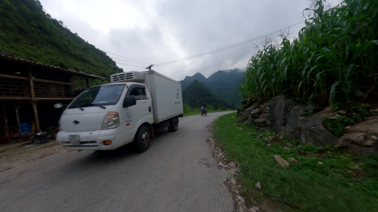 Riding scooter POV through Ha Giang Loop, mountain landscapes with tight curving roads as cars pass in opposite direction