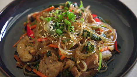 japchae or stir-fried korean vermicelli noodles with vegetables and pork topped with white sesame - korean traditional food style