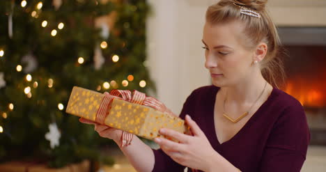 woman shaking christmas present before opening ribbon