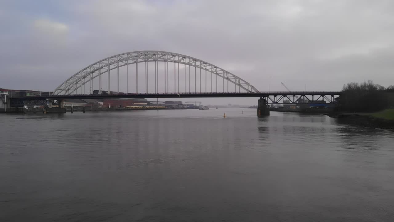 Calm river streaming slowly below a bascule bridge where cars are driving over. Steady dolly drone shot