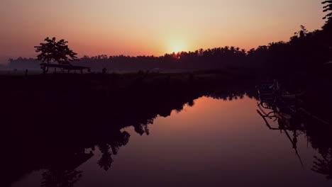 early morning drone footage of a tropical indonesian river shows local fishing boats and golden light reflecting off the calm water, surrounded by thick green jungle