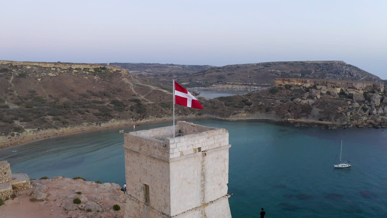 Malteksernes flagg vaier på et steintårn over en bukt, luftfoto.