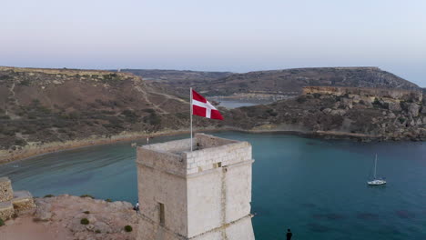 flag of maltese knights flying on a stone tower above a bay,aerial