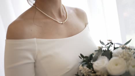bride in off shoulder dress holding bouquet, adorned with a pearl necklace