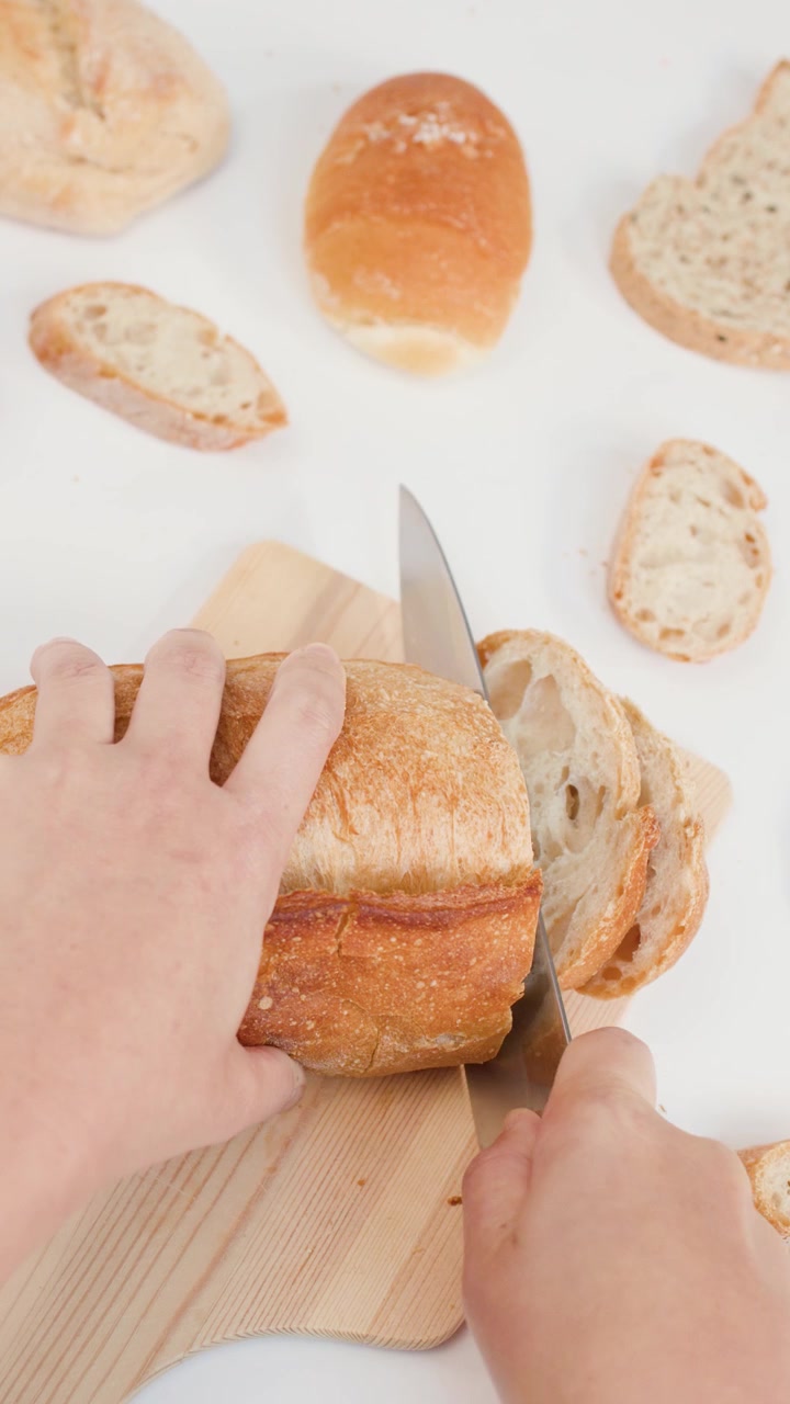 Person Slicing Fresh Loaf of Bread on Wooden Cutting Board
