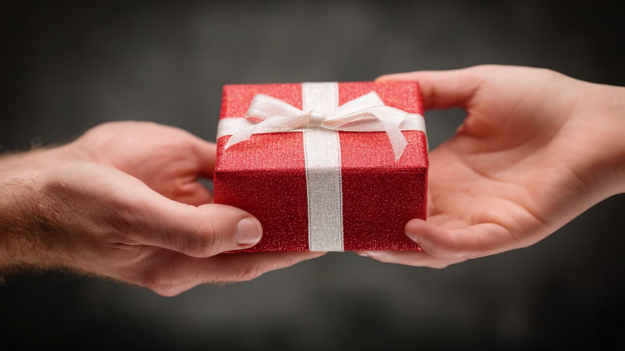 Il passaggio di un regalo rosso splendidamente incartato, immortalato in due fotogrammi, che evidenzia la gioia di donare mentre una mano offre il dono a un'altra.