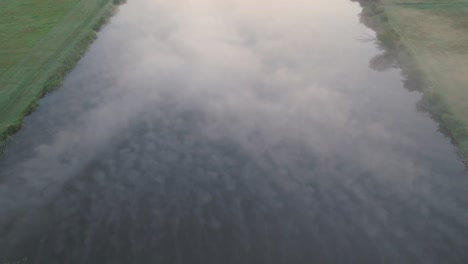 aerial over mist-covered wetlands as dense fog settles at dusk, softening edges and creating a tranquil scene, pullback as mist pushes forward