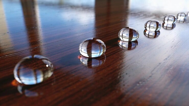 Panning camera following row of water droplets on wood tabletop, highlighting center reflections
