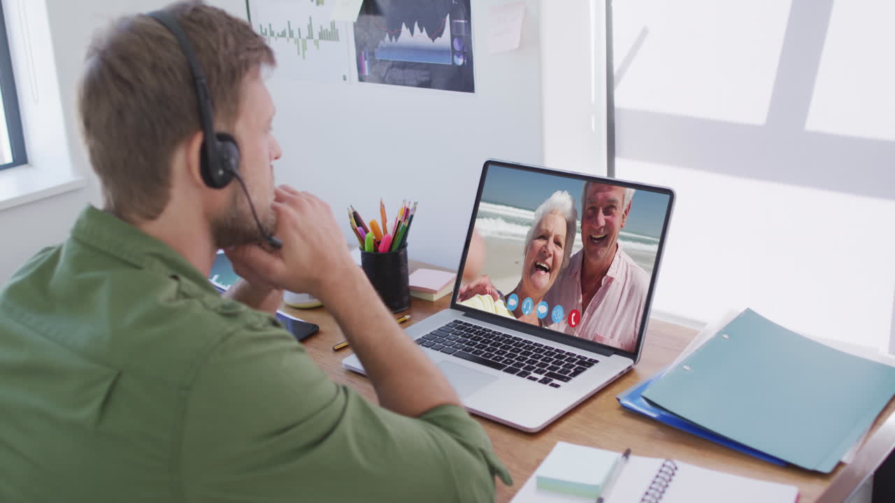 Kaukasisk mand i en videochat på en bærbar computer, iført telefonheadset derhjemme.