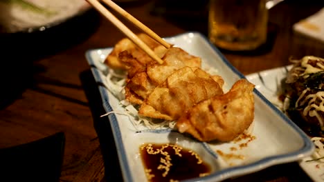 chopsticks picking gyoza from a serving plate