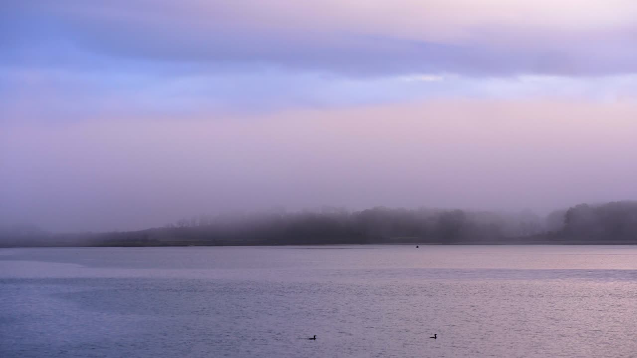 잔잔한 물과 형형색색의 하늘이 있는 일출 시 바다와 해변 마을의 안개