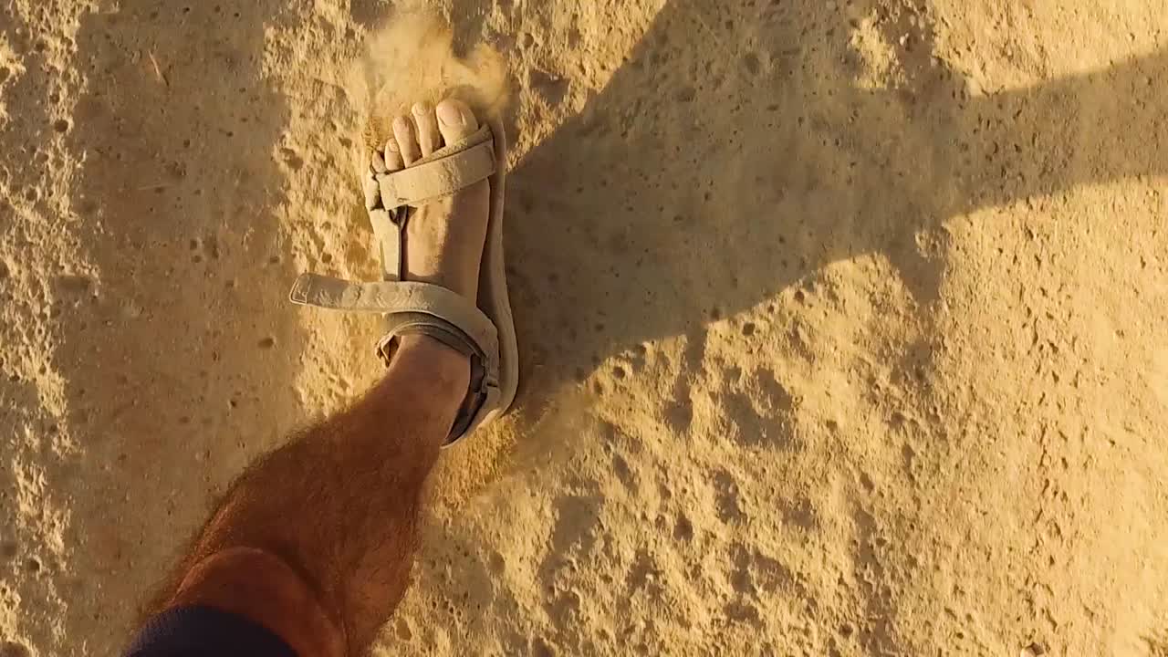 Uomo che cammina con sandali lungo un sentiero sabbioso e polveroso - Punto di vista