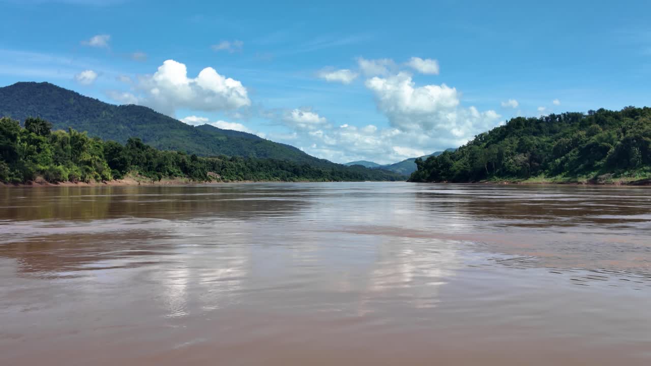 Vista panoramica del fiume Mekong in Laos, scattata da una barca, che mostra le rigogliose foreste verdi, le montagne e il cielo blu