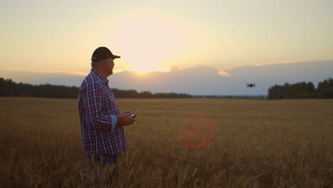 Farmer-holds-remote-controller-with-his-hands-while-quadcopter-is-flying-on-background.-Drone-hovers-behind-the-agronomist-in-wheat-field.-Agricultural-new-technologies-and-innovations.