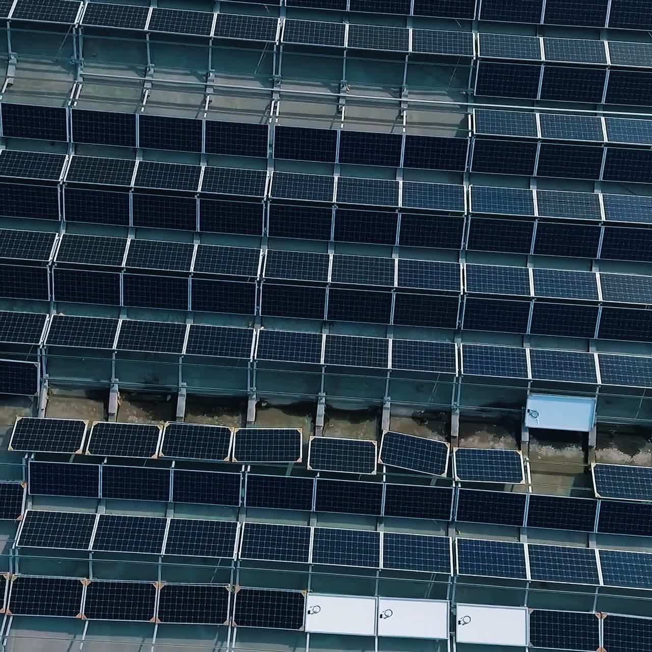 Blue solar panels on roof of building. Construction of innovative photovoltaic solar cells. Alternative source of energy. Camera moving down. Aerial view