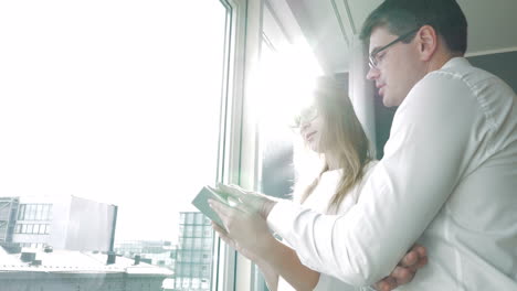 Young-happy-businesspeople-with-pad-by-the-window