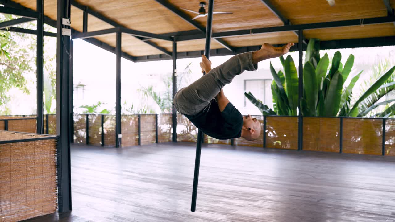 Uomo che esegue una routine di pole dance acrobatica in uno studio all'aperto