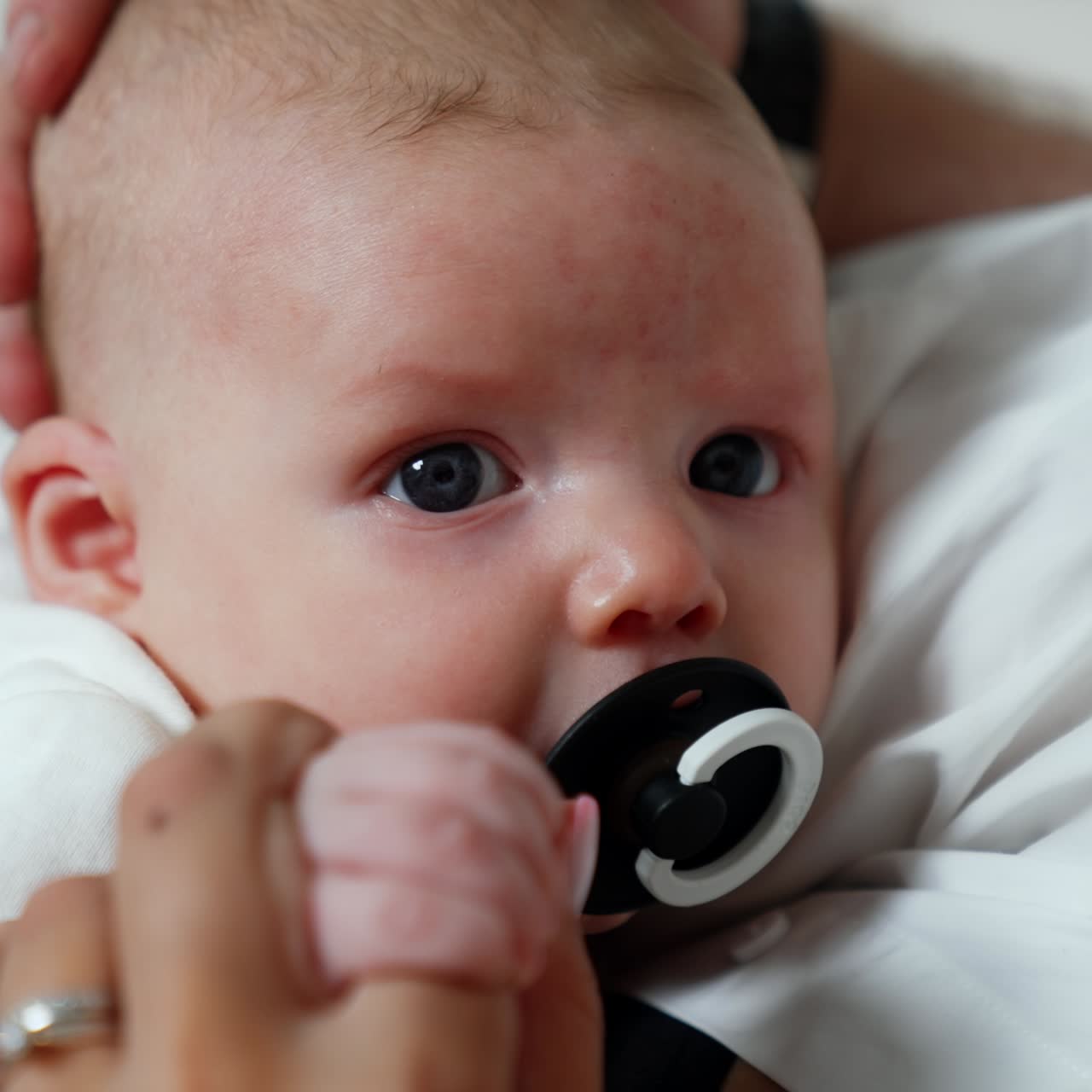 Beautiful grey-eyed Caucasian newborn in mom's arms. Baby lies peacefully suckling the pacifier. Close up