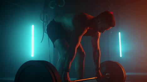 muscular fitness man doing push a barbell over his head in modern fitness center. functional training. snatch exercise. slow motion color led light saturated bright colors