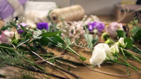 View-from-above:-wooden-table-with-flowers,-scissors,-tapes,-decorating-paper-and-other-tools-for-bouquet-arrangement-at