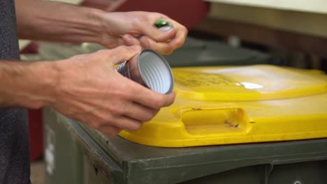 Person-removes-label-from-tin-can,-puts-can-in-recycle-bin-and-label-in-trash-bin