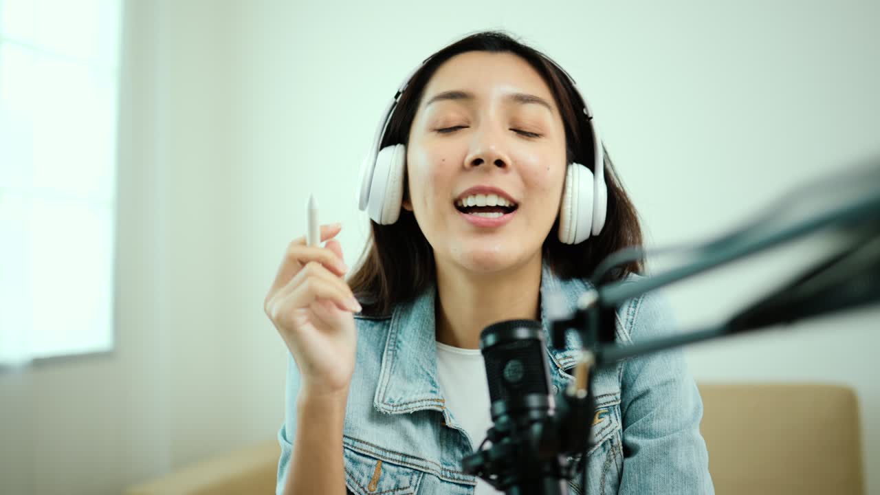 컨텐츠 제작자 여성 호스트는 헤드폰과 마이크로 노트북에서 캐스트를 스트리밍하고 방송 스튜디오에서 게스트 대화를 응원합니다.