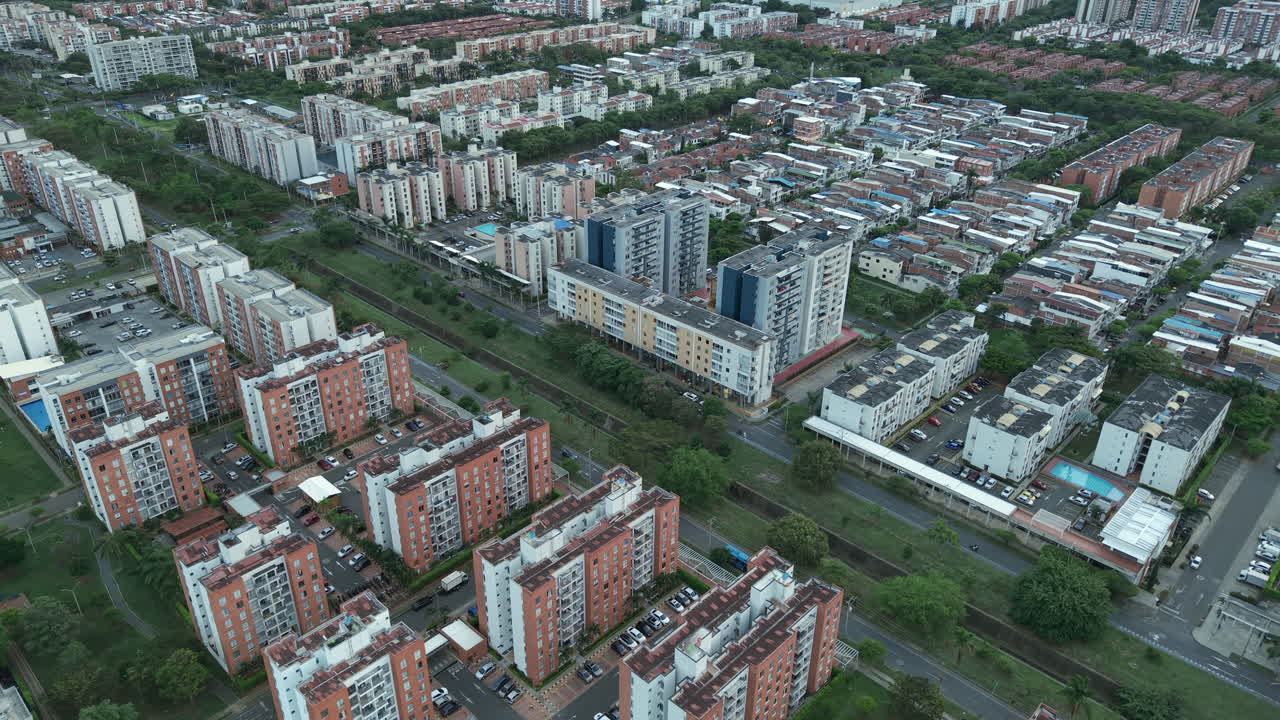 Drone footage captures sprawling residential buildings in Valle del Lili, Cali. Overcast lighting highlights the urban grid and lush greenery amid the city's vibrant architecture