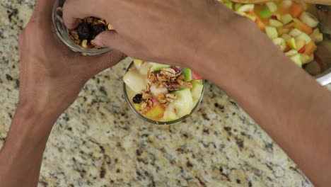 overhead view of a man adding granola to fruit cocktail