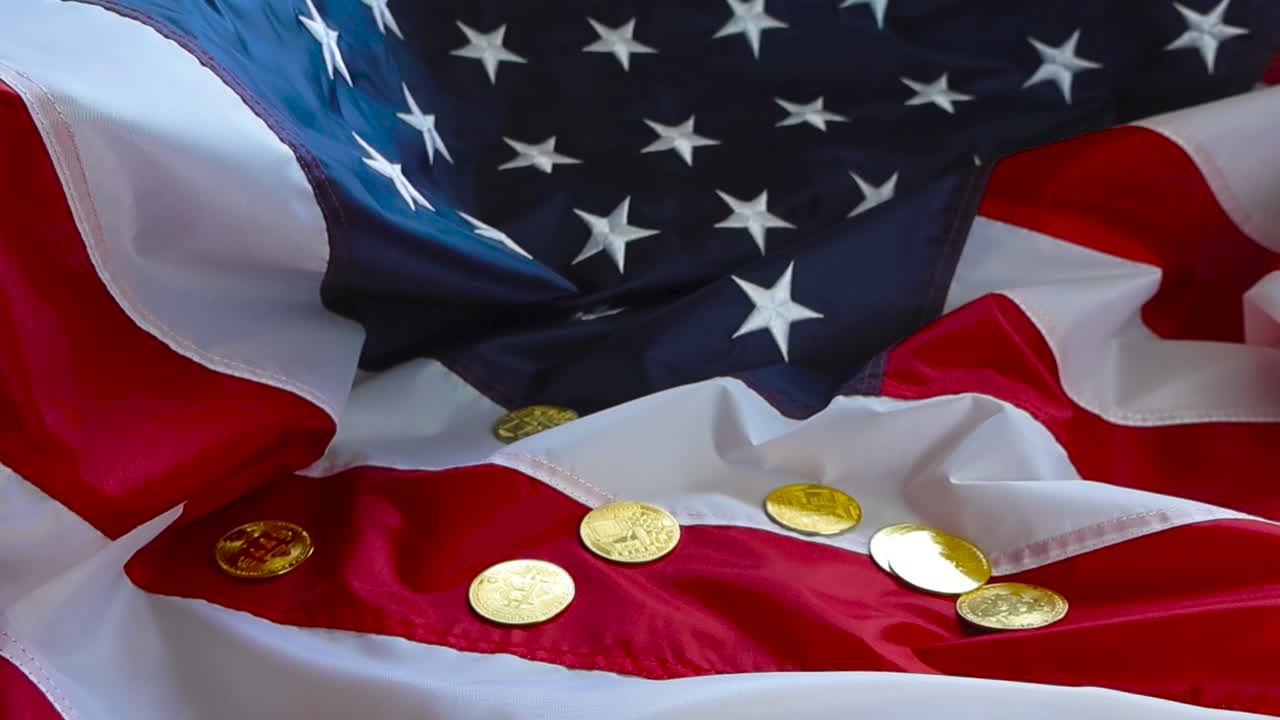 Golden shiny and reflective Bitcoin cryptocurrency coins fallin in slow motion on a United States of America flag that is vbrant red and blue colored. Coins fall and spin in a cinematic way.