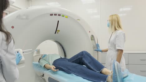 female patient is undergoing ct or mri scan under supervision of two qualified radiologists in modern medical clinic. patient lying on a ct or mri scan bed, in protective mask moving inside the machine.