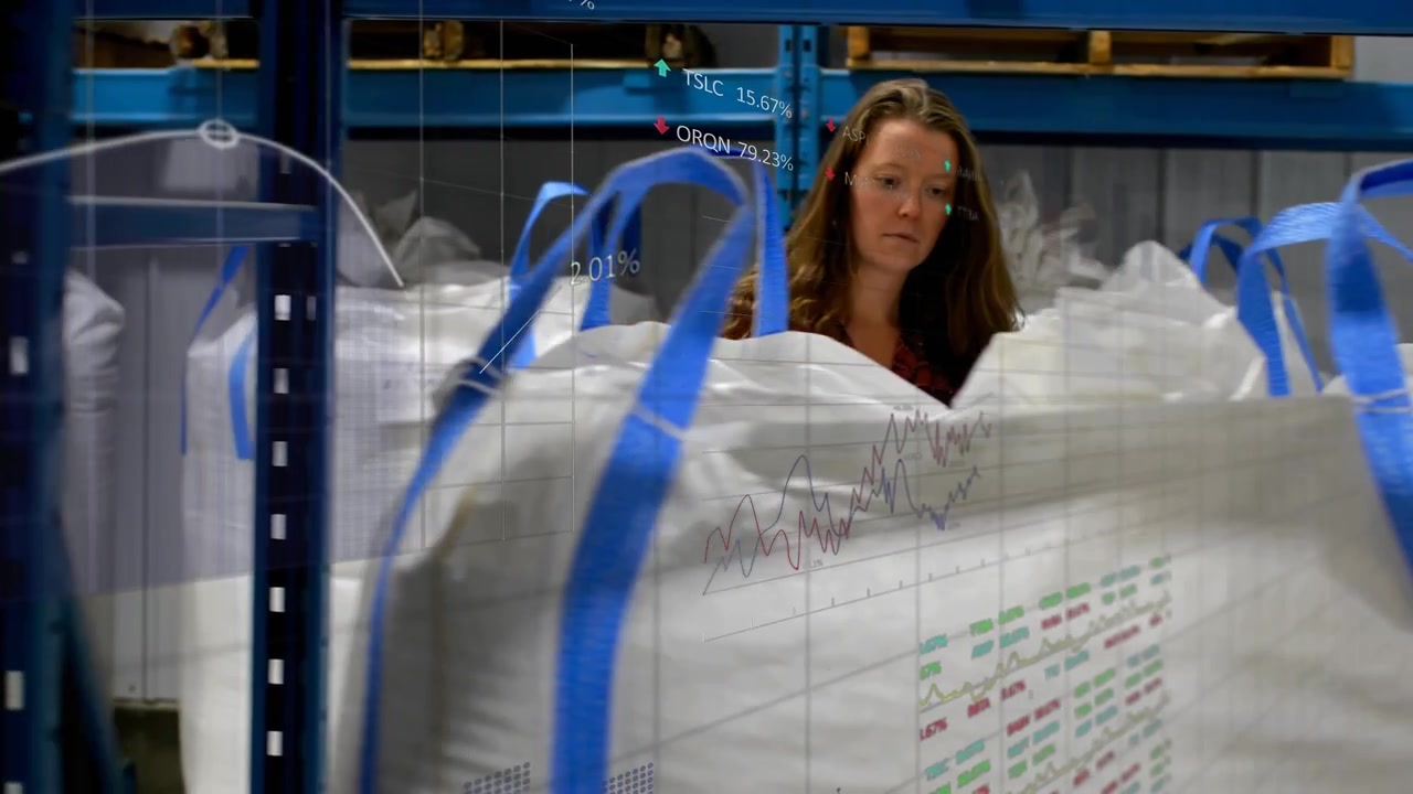 Depot worker walking aisle among bulk bags scanning label via scanner showing tags for audit