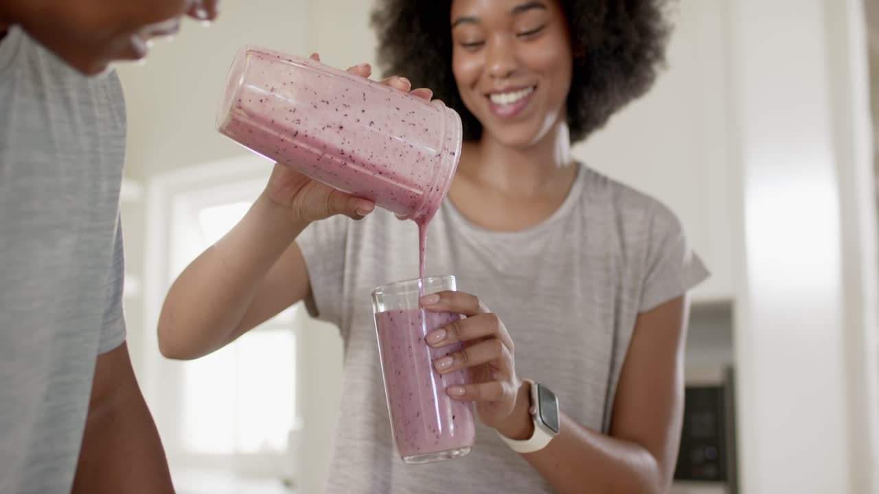 Mutfaktaki Afrikalı Amerikalı çift smoothie alırken, kadın kavanozu eğerek erkeğin bardağına dolduruyor.