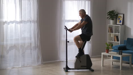 Entrenamiento-En-Casa-Con-Una-Moderna-Bicicleta-Estática-Para-Perder-Peso-Y-Mantenerse-En-Forma-De-Un-Hombre-De-Mediana-Edad-En-La-Sala-De-Estar