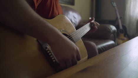 man's hands as he strums an acoustic guitar in a living room as wind blows the curtains in the background