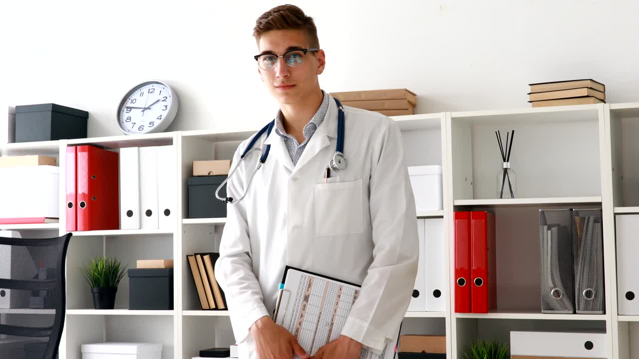 İş yerinde elinde not defteriyle kameraya bakan genç doktor
