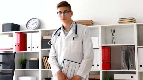 young doctor with clipboard in hands looking at camera in workplace