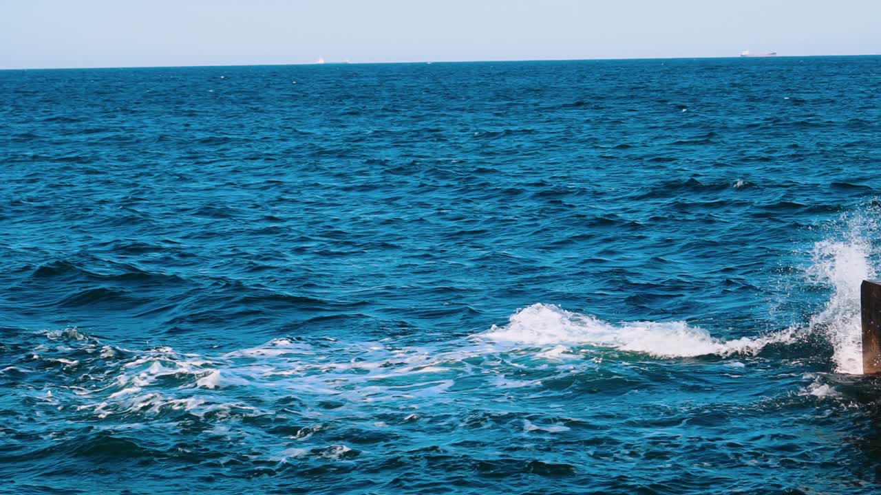 Amazing water background. Waves swaying on the sea water. Beautiful blue water waves with white foam crashing on the dock. Slow motion.