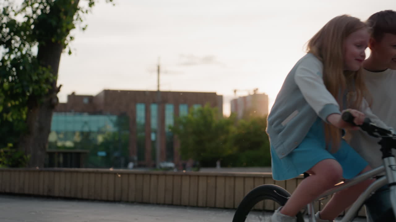 summer brother teaching sister to ride bicycle on wooden path under warm sunset glow, urban buildings in distance, dust motes shimmering in golden light, sibling support and joyful learning moment