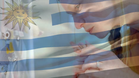 animation of uruguayan flag over caucasian mother kissing feet of baby