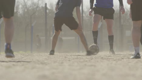 people play football soccer on a dusty field as the afternoon sun shines bright in the background