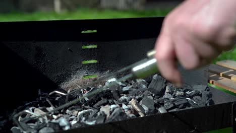 preparing coal with food tongs in a barbecue outside on a sunny day