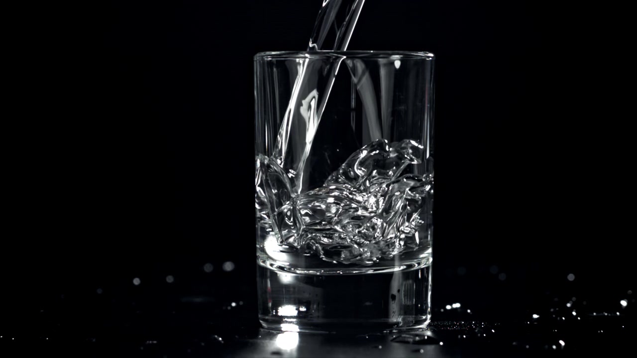 Hælder vand i et klart glas på sort baggrund i slowmotion