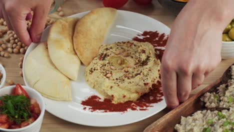 israeli cuisine. putting plate with hummus decorated with paprika and pita close-up. national food, middle eastern culture. vegan chickpea puree snack. appetizer made from mashed chickpeas