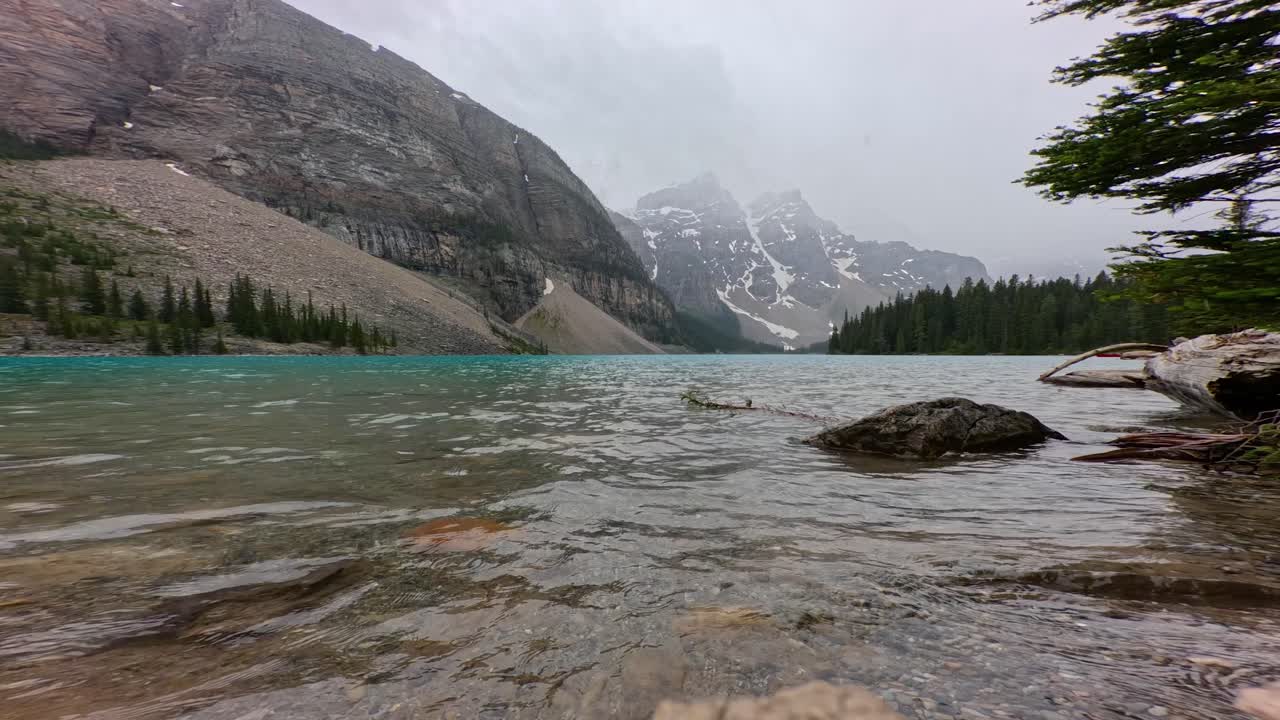 Moraine lake on a foggy and rainy summer day. Video from close to the water and the glacier covered mountains in the background