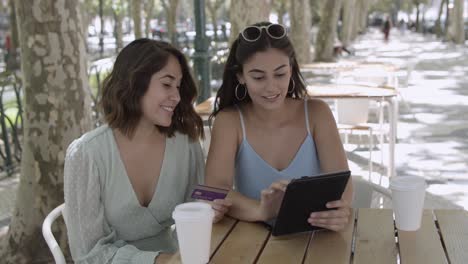 amigas felices sentadas en un café de la ciudad y usando una tableta