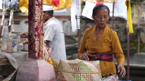 Una-Anciana-Balinesa-Ayuda-A-Cuidar-Los-Altares-En-Un-Templo-Hindú-De-Bali,-Indonesia,-Reemplazando-El-Incienso