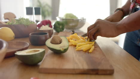 slicing mango on wooden cutting board with avocado and vegetables nearby