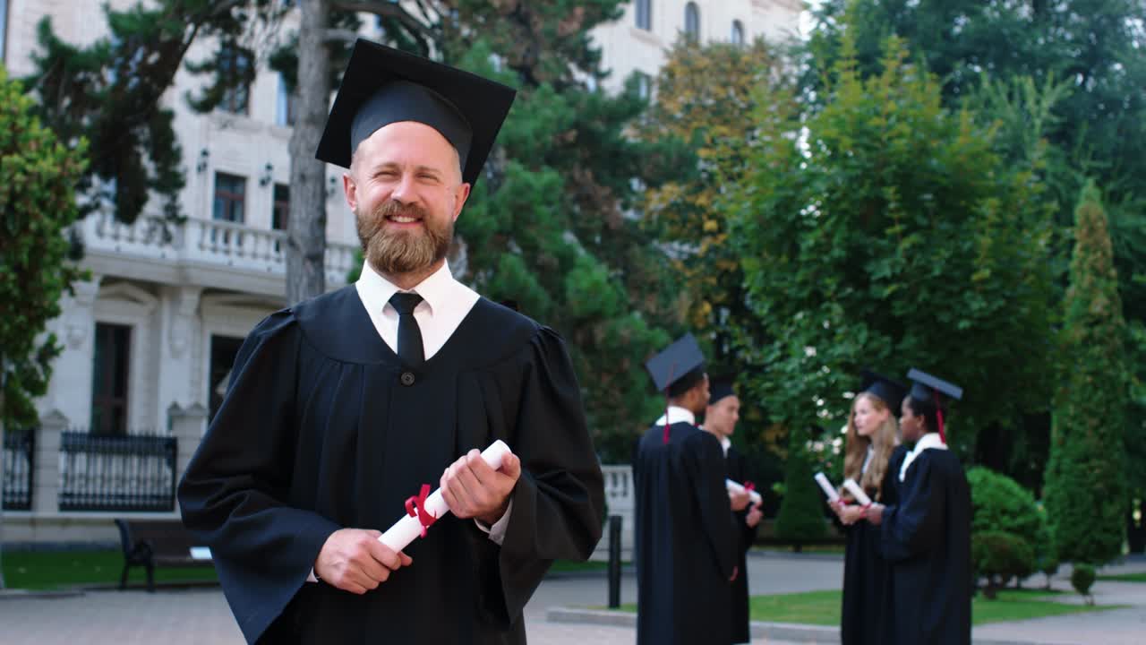 Charismatic man in the college garden posing in front of the camera after his graduation he wearing a graduation suit and cap and holding diploma