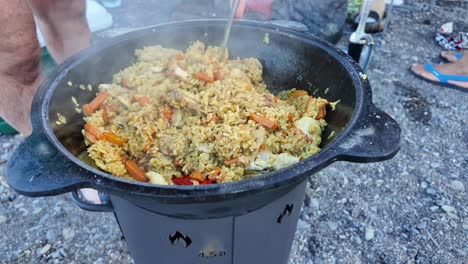 una gran olla de pilaf está siendo agitada con una cuchara de madera